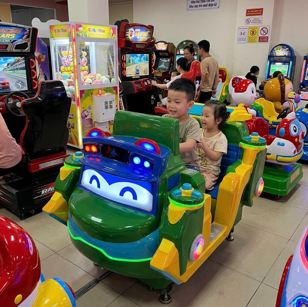 Hai bé đang vui chơi trên máy bay nhún điện tại khu vui chơi trong nhà, máy có khoang ngồi rộng rãi cho 2 người, trang bị màn hình và âm thanh sinh động